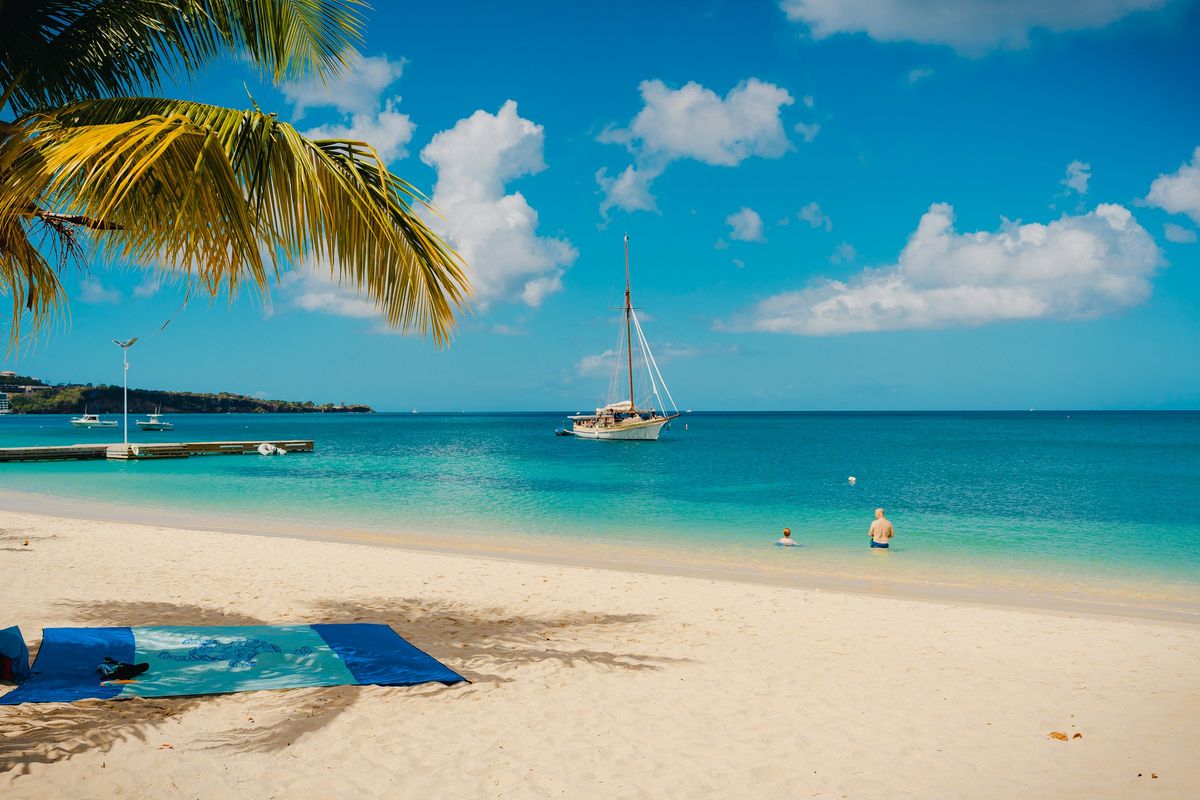 A sailboat on turquoise water near a sandy beach