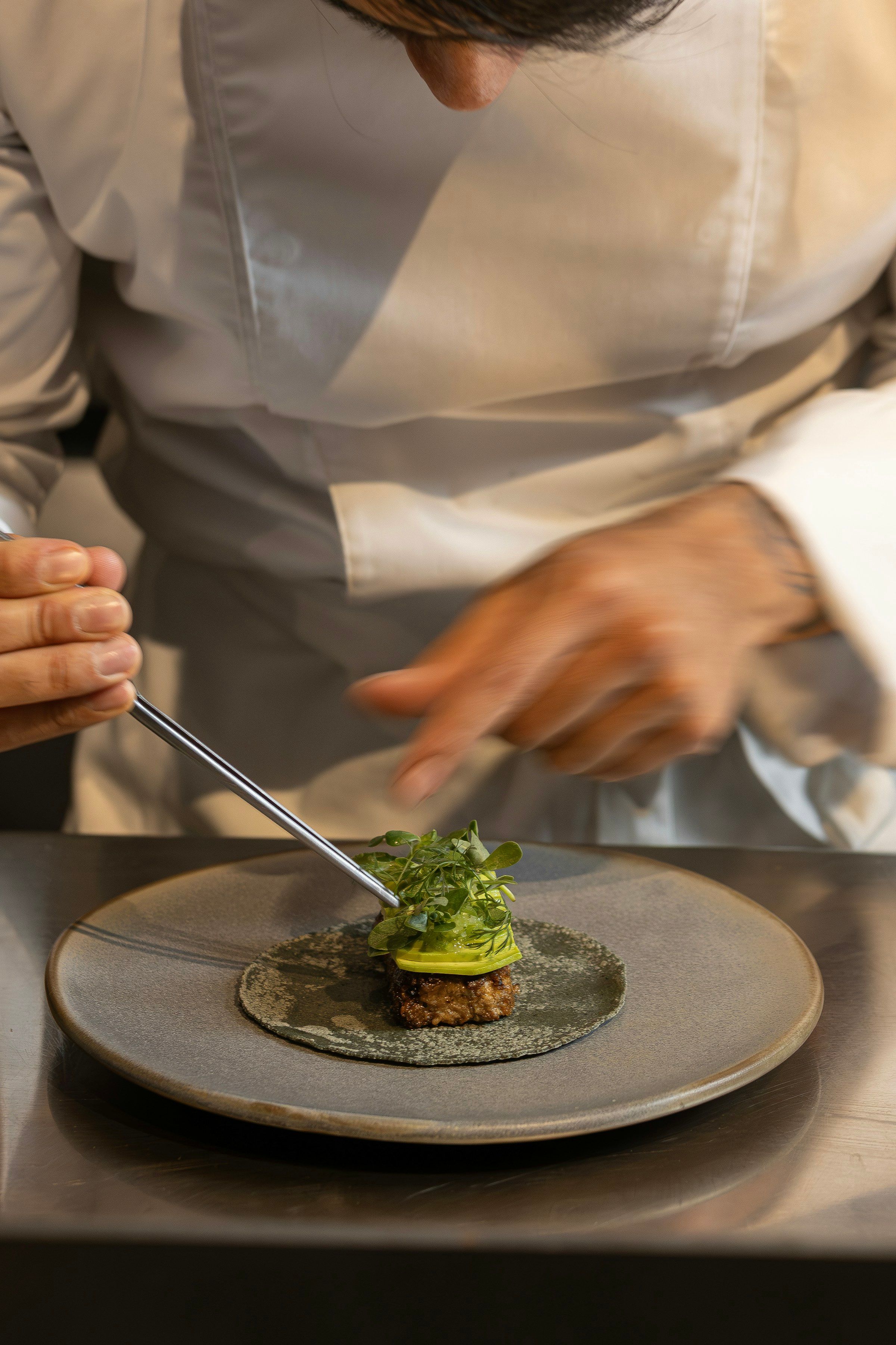 A chef plating a gourmet dish with tweezers