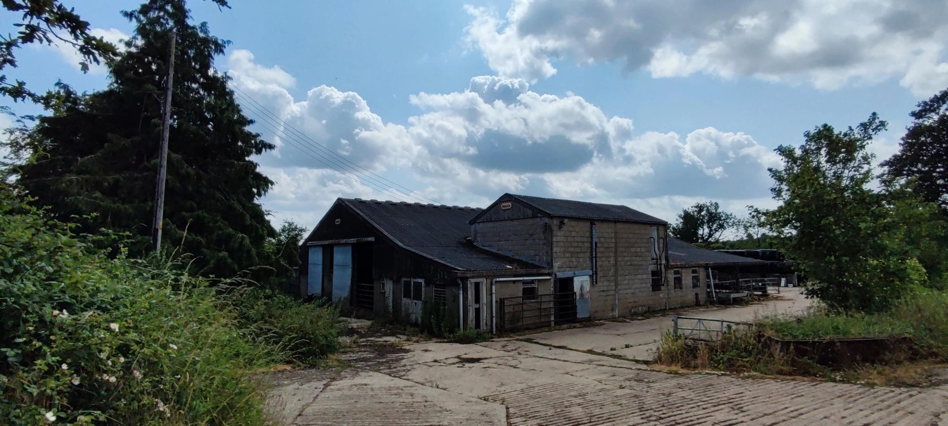 Farm buildings for renovation by Studio Bark with blue sky background and hedgerows