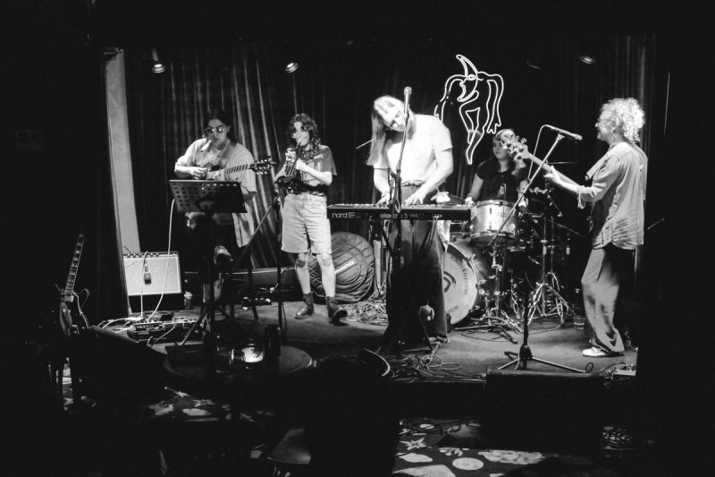 band playing on stage. drummer, keys, guitar, bass, and trumpet player