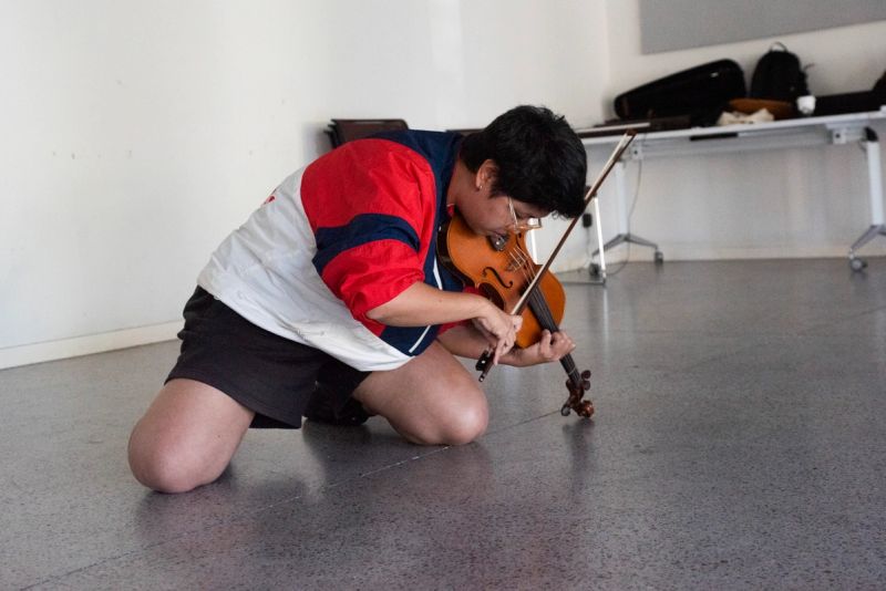 Attendee playing violin expressively while kneeling on ground .