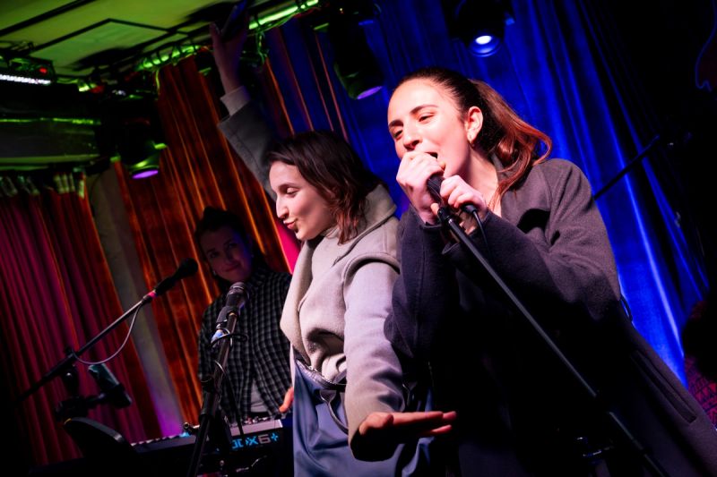 two jammers on stage, one singing and one with arms out expressively. keys player in background watching