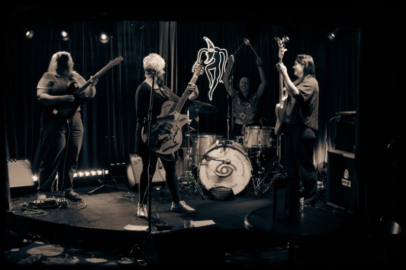 photo of full band on stage looking at one another, drummer holding sticks above them in the air