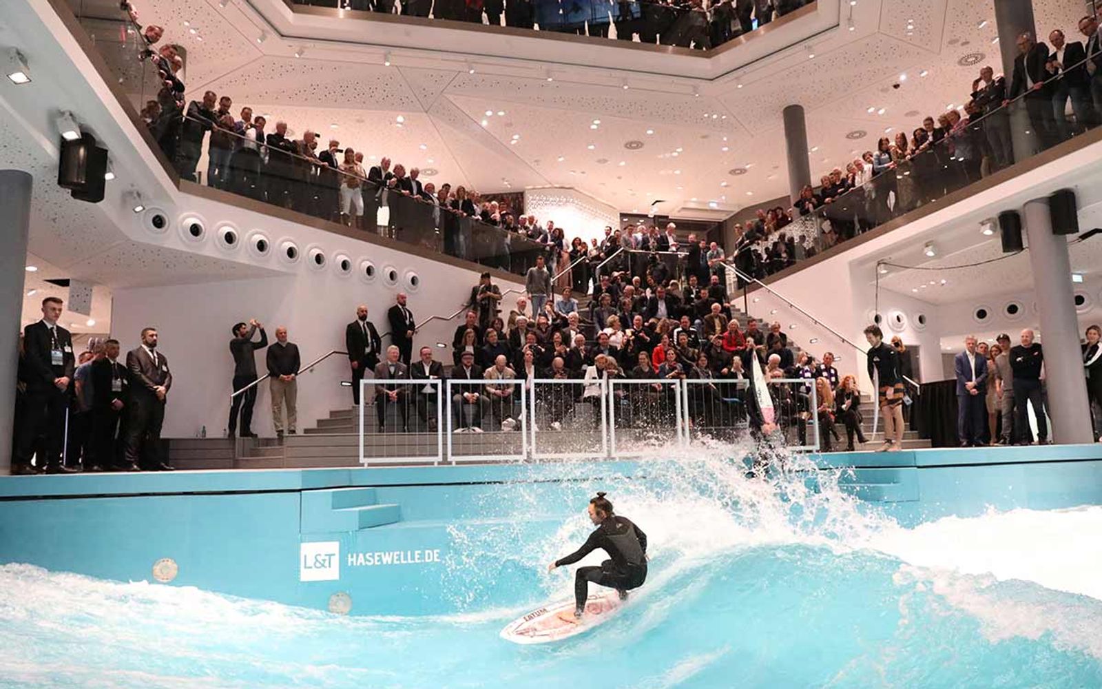 A surfer on the Hasewelle in front of a full gallery of spectators.