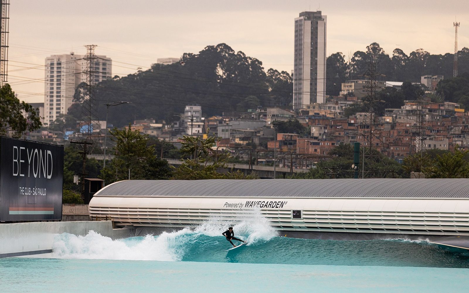 A surfer on Beyond The Club's lagoon, with São Paulo's towers and hillside homes behind.