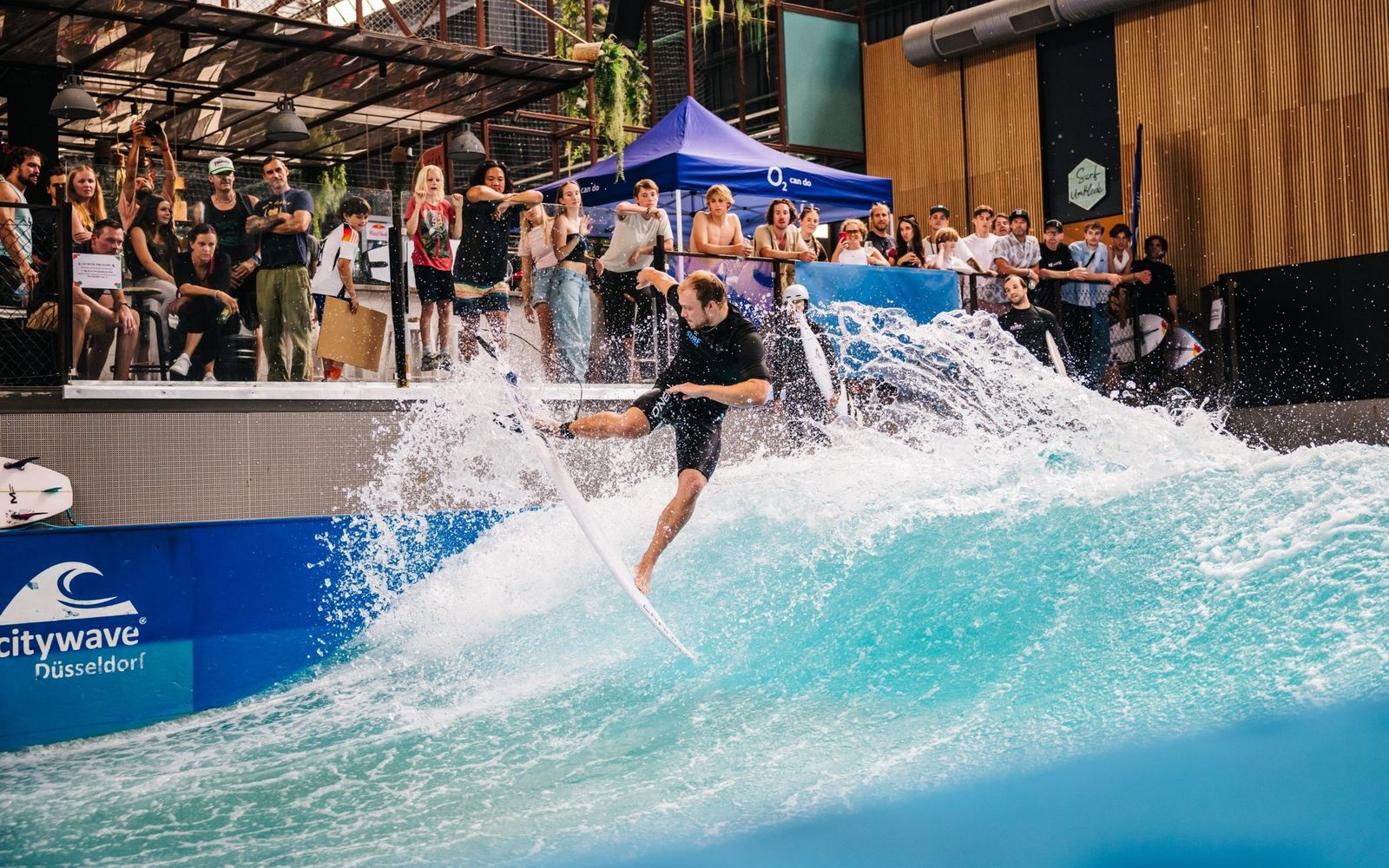 A surfer throws spray in front of a crowd at RheinRiff's indoor wave.