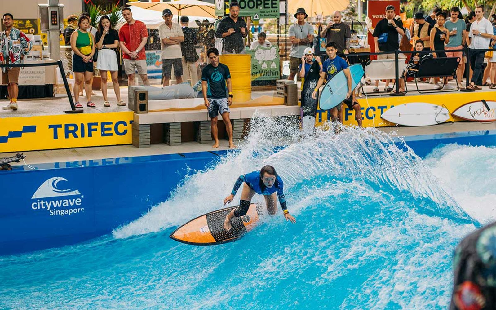 A surfer on TRIFECTA's Citywave in Singapore, with spectators on the deck above.
