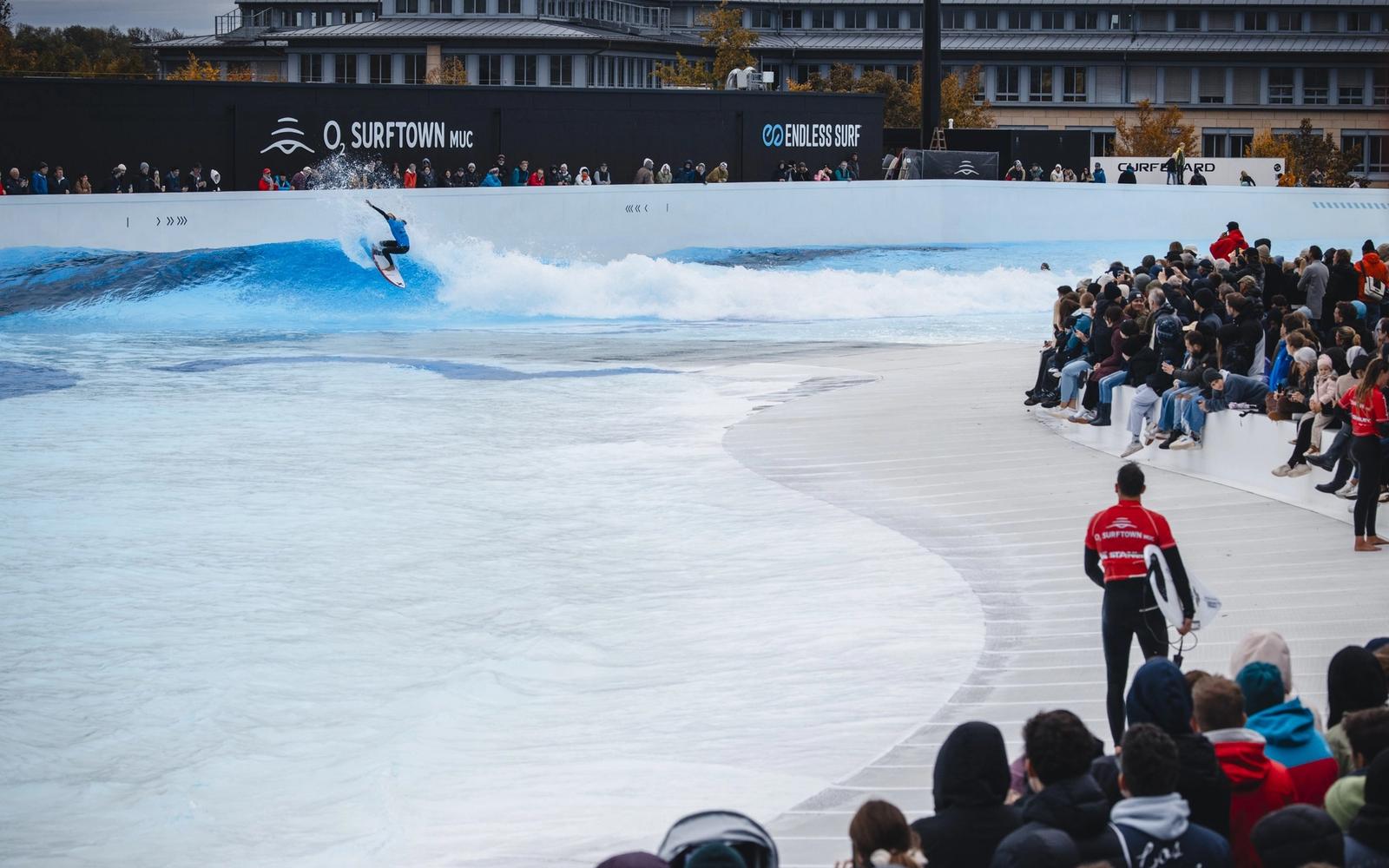 Spectators packing the beach at O2 SURFTOWN MUC while a surfer rides the lagoon.