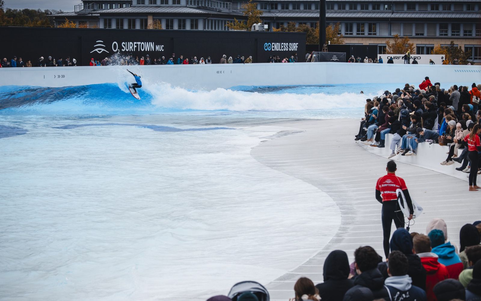 Spectators packing the beach at O2 SURFTOWN MUC while a surfer rides the lagoon.