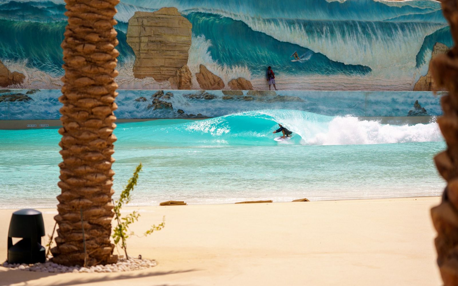 A surfer on the Surftopia lagoon at Aquarabia, below its painted wave mural.