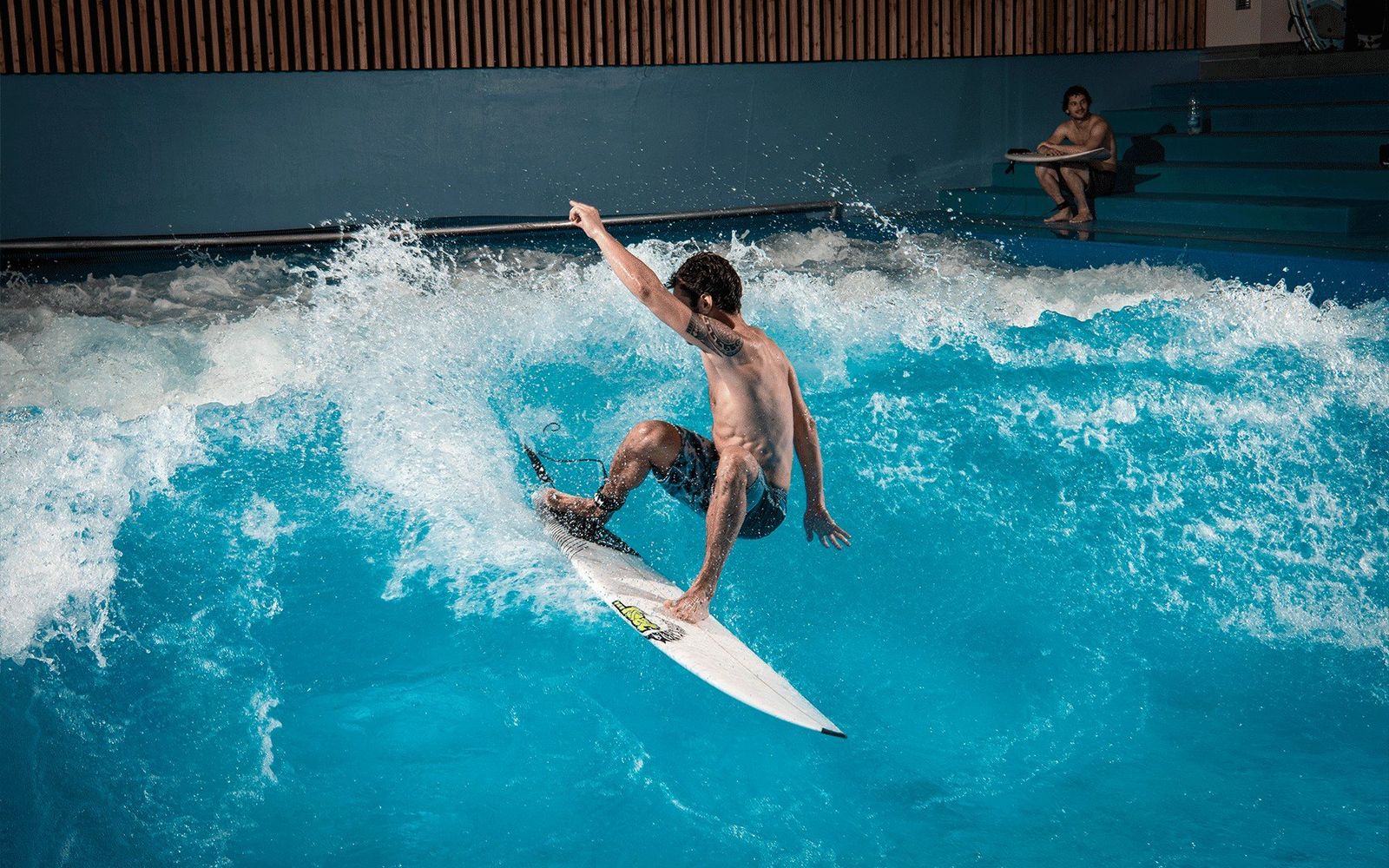 A surfer turning on OANA's indoor standing wave, with the spectator seating behind.
