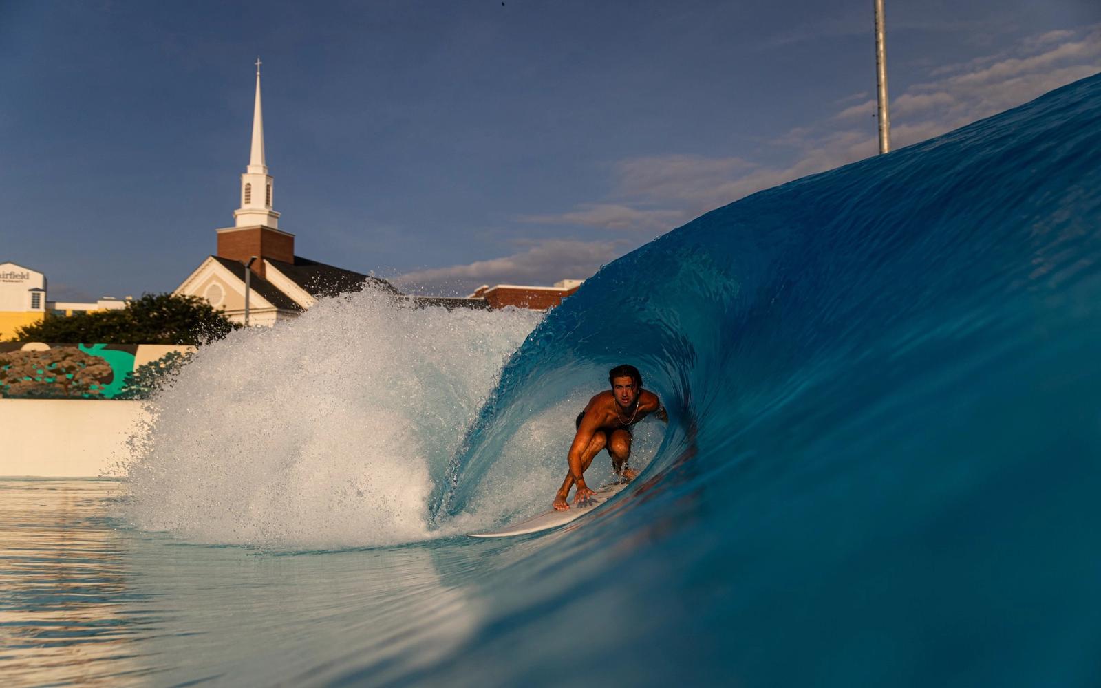 A barrel at Atlantic Park, with Virginia Beach rooftops and a church steeple behind the lagoon wall.