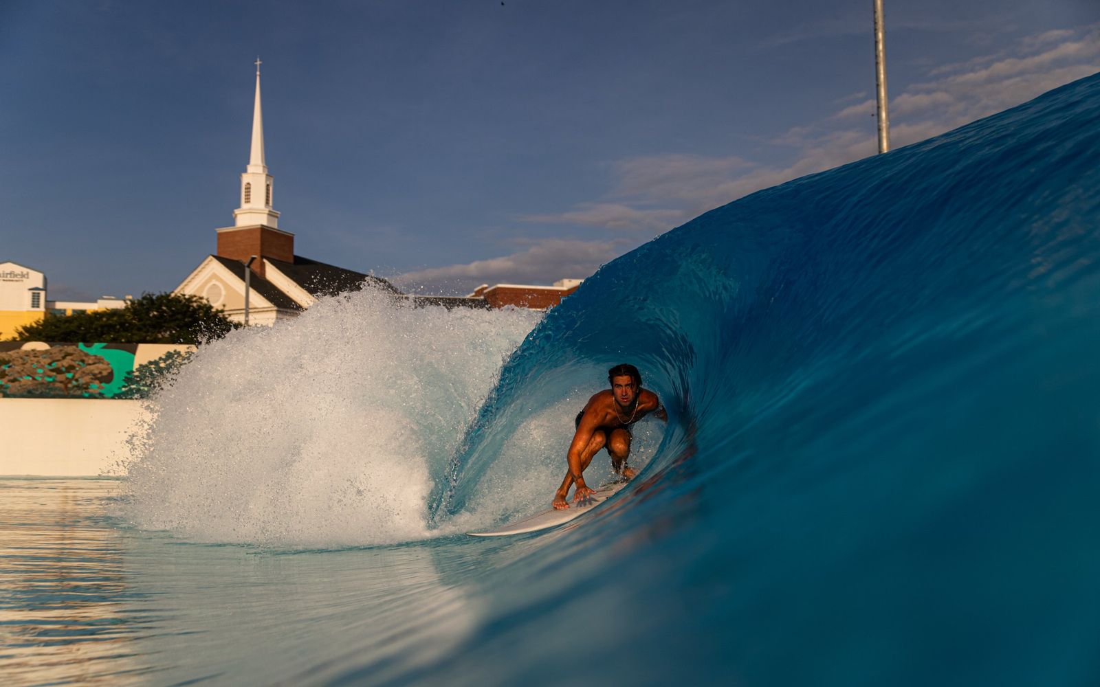 A barrel at Atlantic Park, with Virginia Beach rooftops and a church steeple behind the lagoon wall.