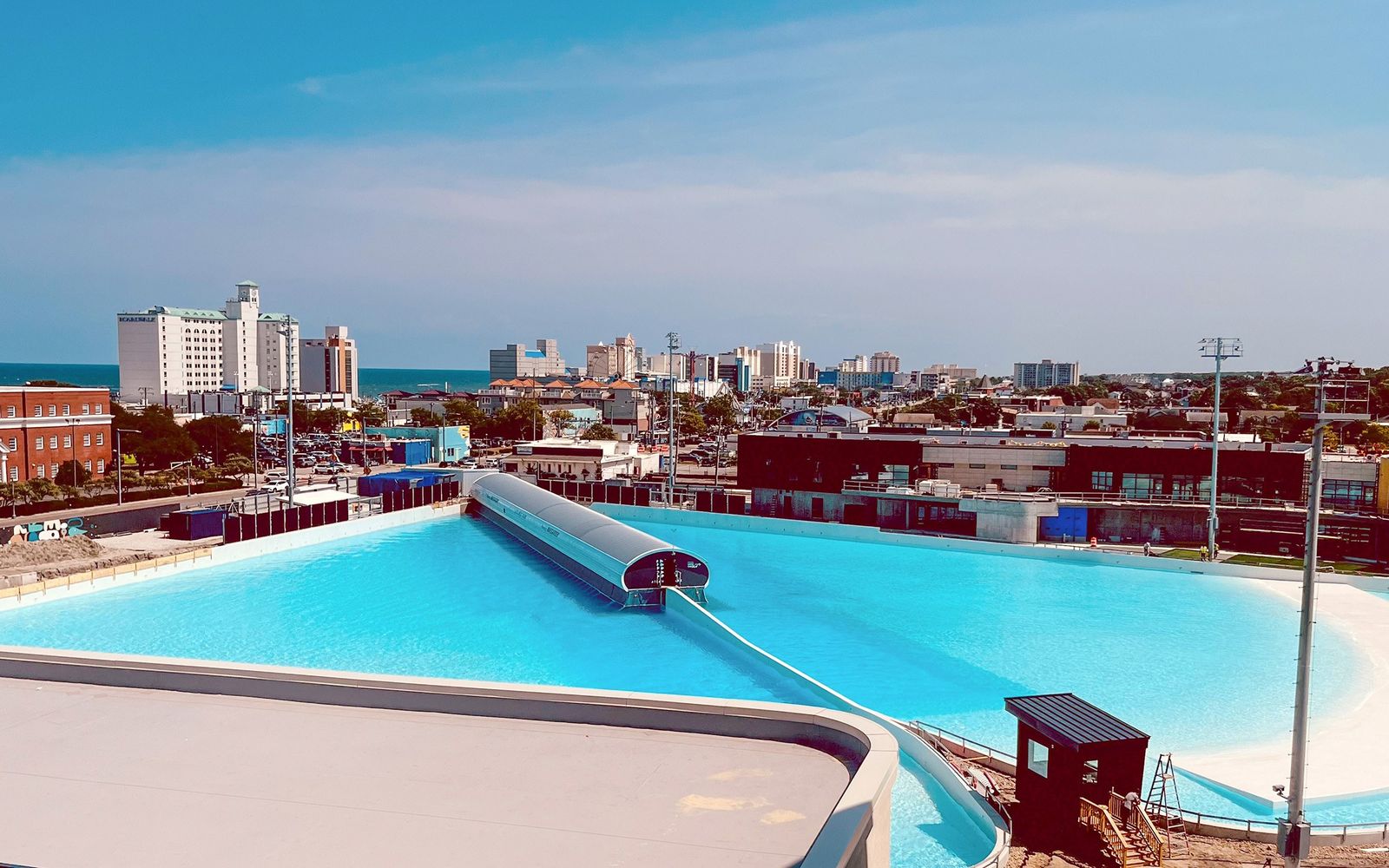 Atlantic Park's lagoon from above, with the Virginia Beach oceanfront hotels and the Atlantic behind.