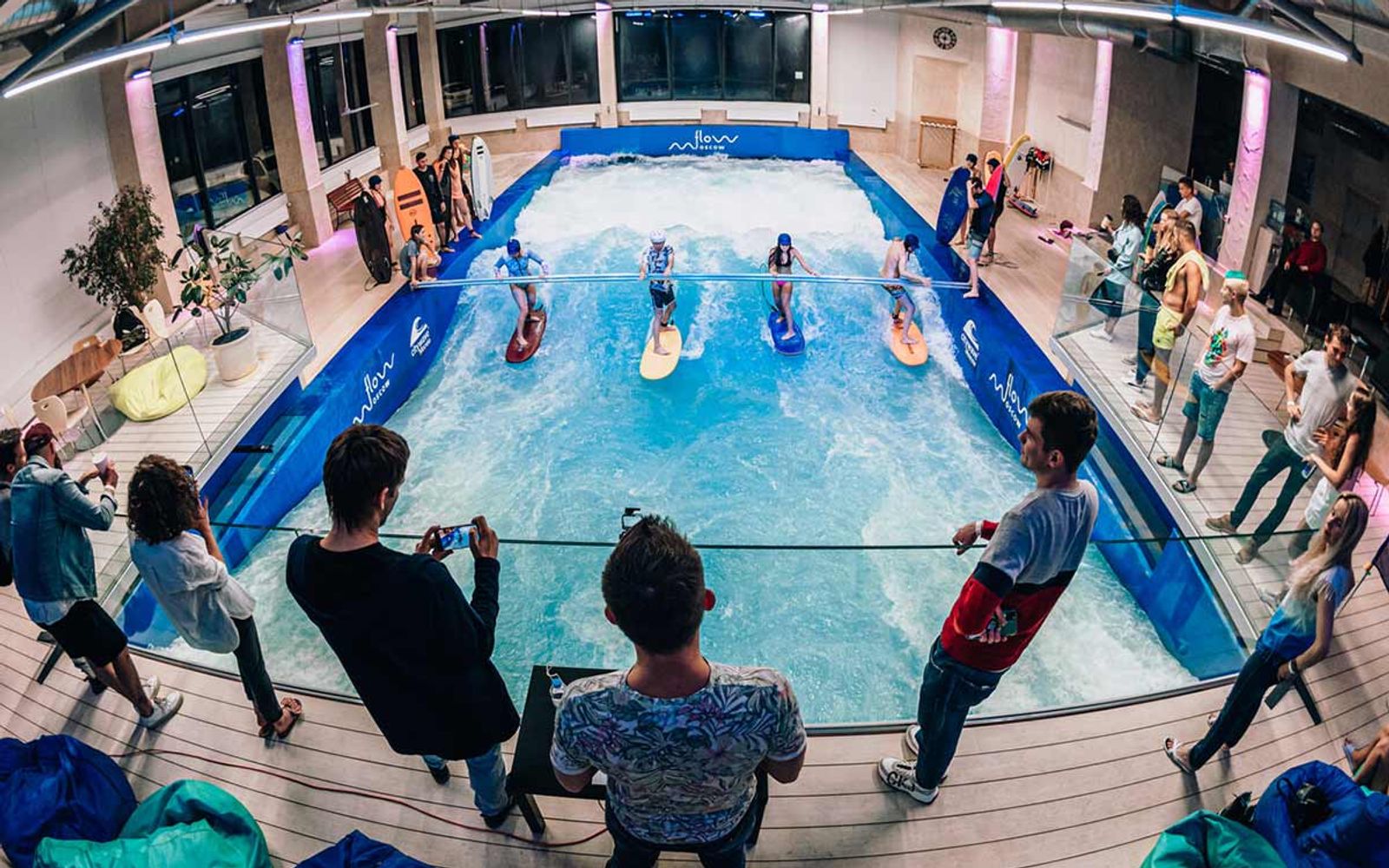 The Flow Moscow wave hall from the poolside, with surfers queuing and spectators along the rail.
