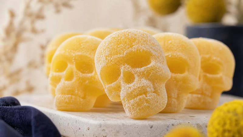 Macro close-up of sugar-coated skull-shaped gummy sweets in rows, one tilted forward in focus.