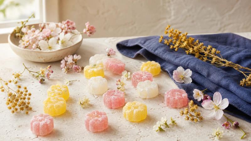 Pastel flower-shaped gummy candies scattered among small fresh spring flowers.