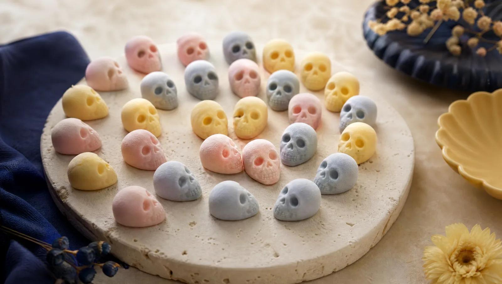 Matte pastel foam skull sweets arranged in a loose spiral on cream stone.