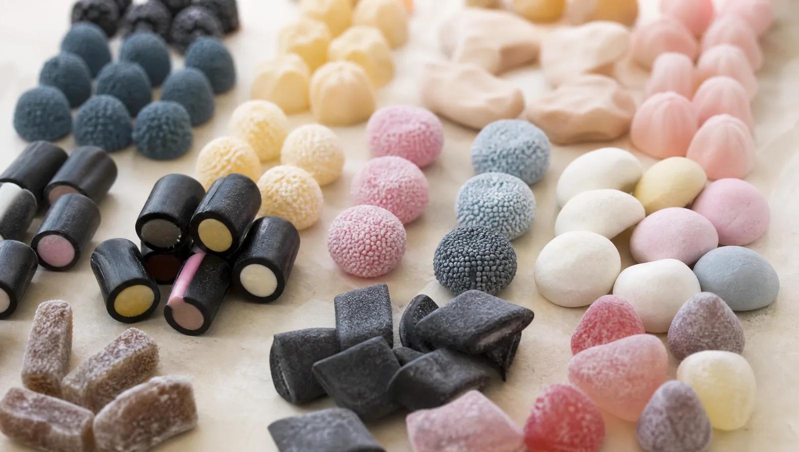 Liquorice pieces, sugared gummies and pastel foam sweets grouped in soft rows.