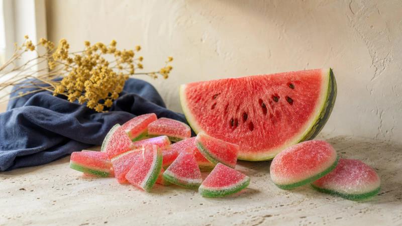 Sour watermelon-slice gummies and oversized watermelon candies next to a fresh watermelon wedge.