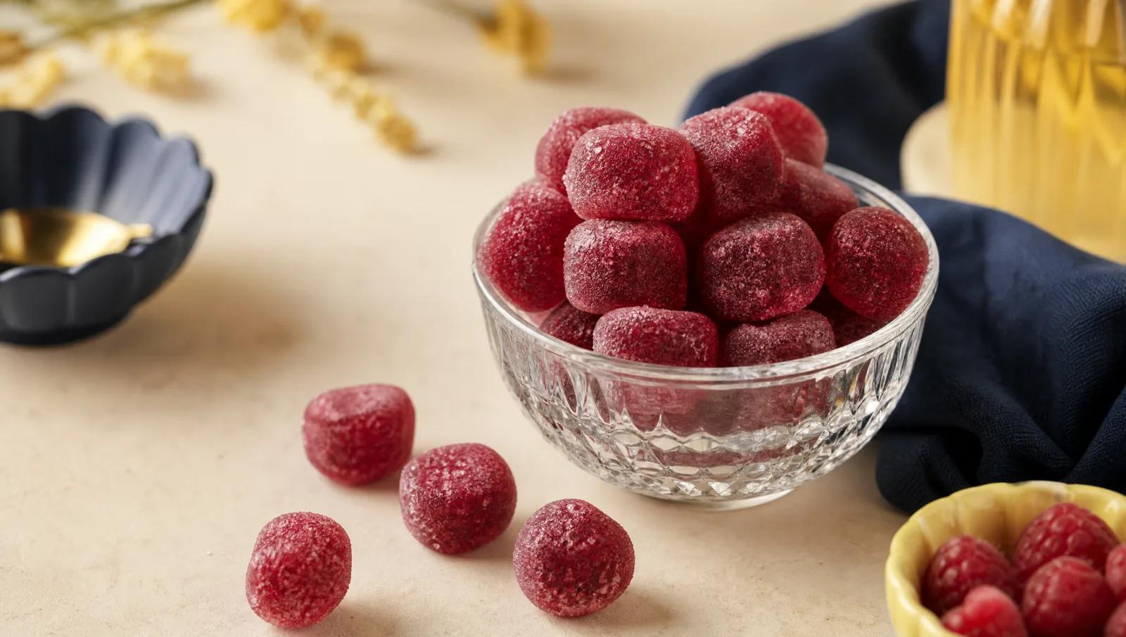 Deep red raspberry sour shot sweets in a small glass bowl, a few spilled beside it.