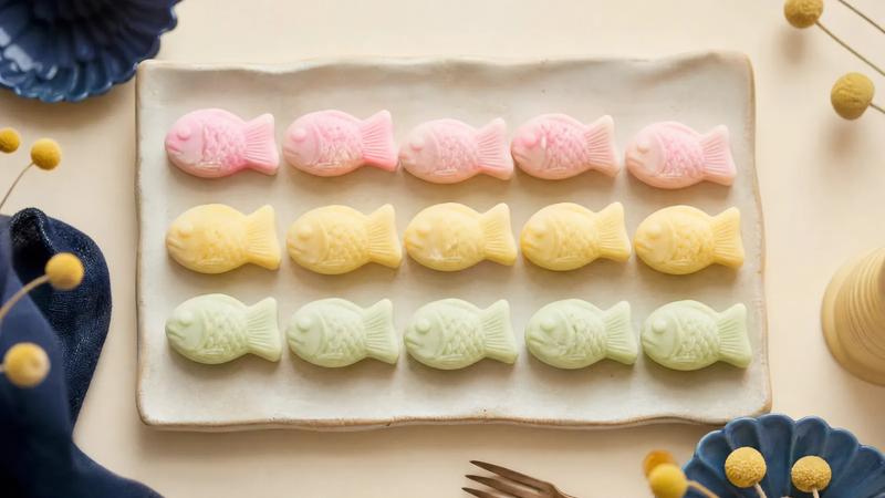 Pastel-coloured fish-shaped sweets in soft pink, yellow and green, overhead rows.