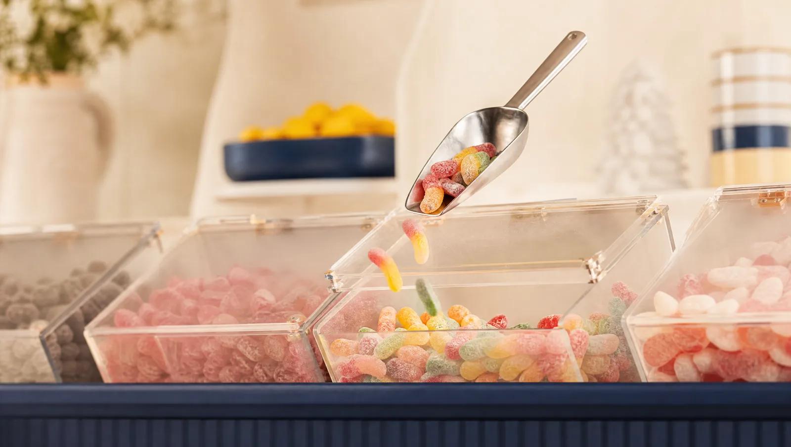 Row of pick-and-mix scoop bins with a scoop mid-air over an open bin.