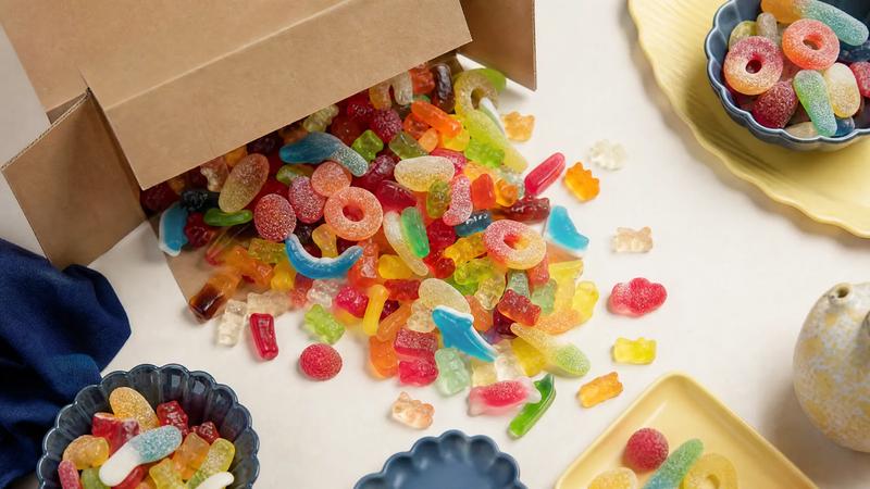 Mixed gummy sweets spilling from an open plain shipping carton.