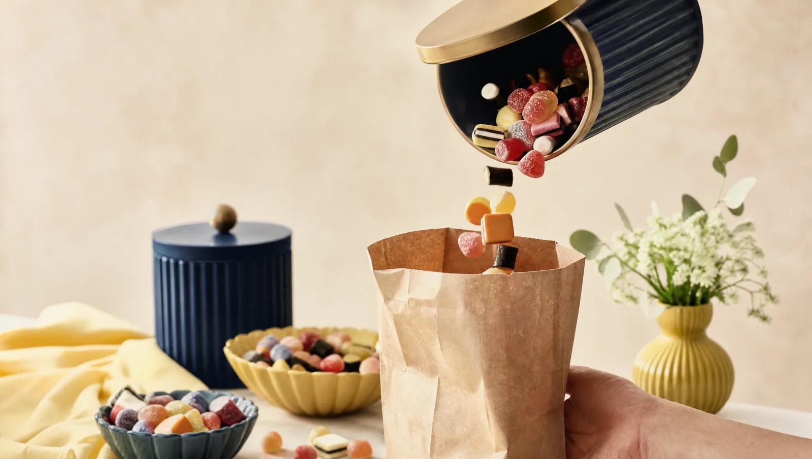 Paper bag being filled from an open bin, sweets mid-pour.