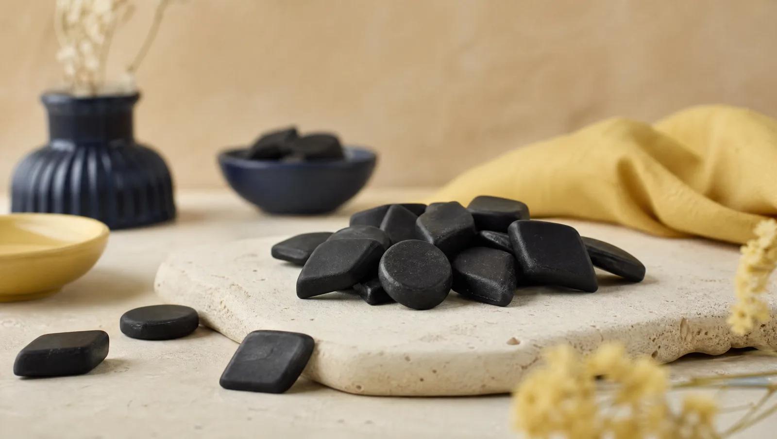 Matte black salty liquorice diamonds and coins scattered on pale stone.