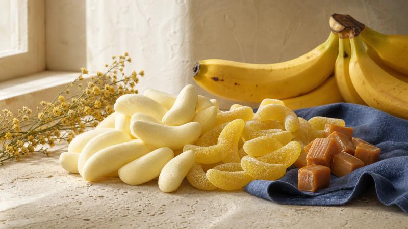 Banana-shaped foam candies and sugar-dusted banana gummies next to a bunch of ripe bananas.