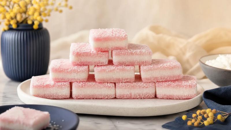 Pastel pink and white layered coconut licorice squares stacked in neat rows.