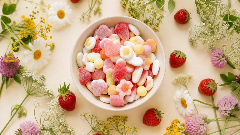 A bowl of candy with summer flowers and strawberries
