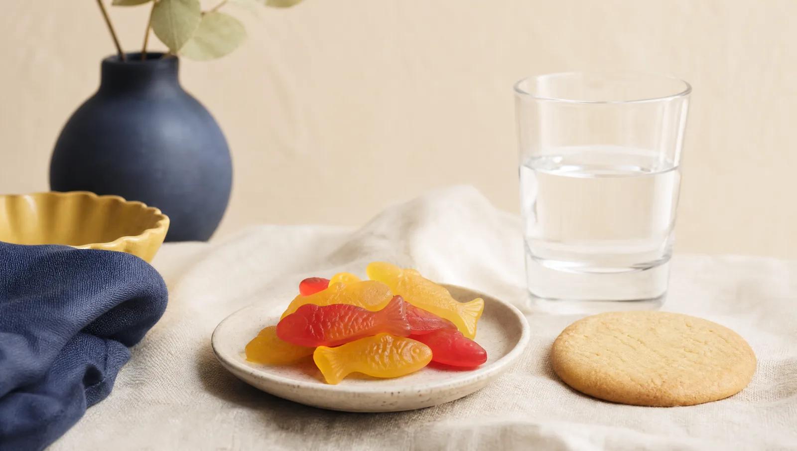 Fish-shaped gummies beside a plain unbranded cookie and a plain drinking glass, still life.