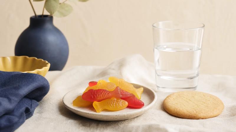 Fish-shaped gummies beside a plain unbranded cookie and a plain drinking glass, still life.