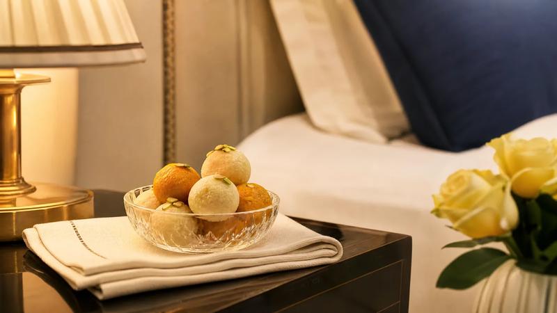Small glass bowl of sweets on a hotel nightstand with folded linen, warm lamp light.