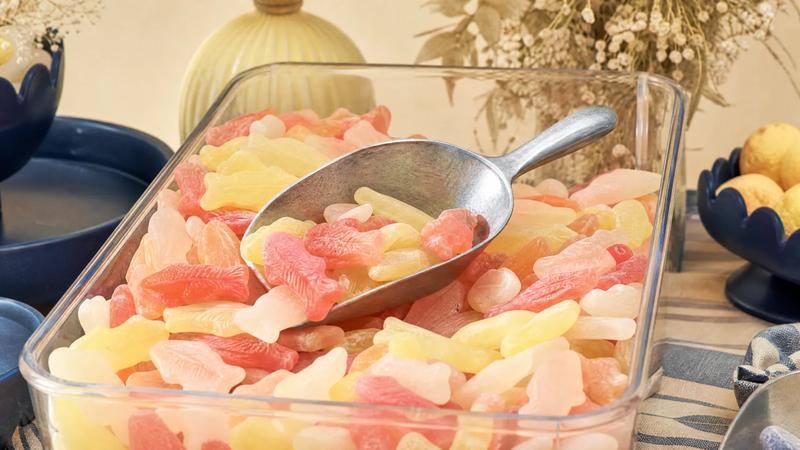 Bulk fish-shaped sweets filling a retail scoop bin, scoop resting on top.
