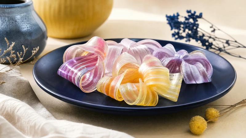 Delicate folded ribbon candy in translucent pastel stripes on a dark plate.