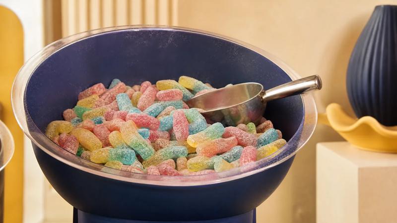 Retail scoop bin filled with sour sweets, scoop resting inside.