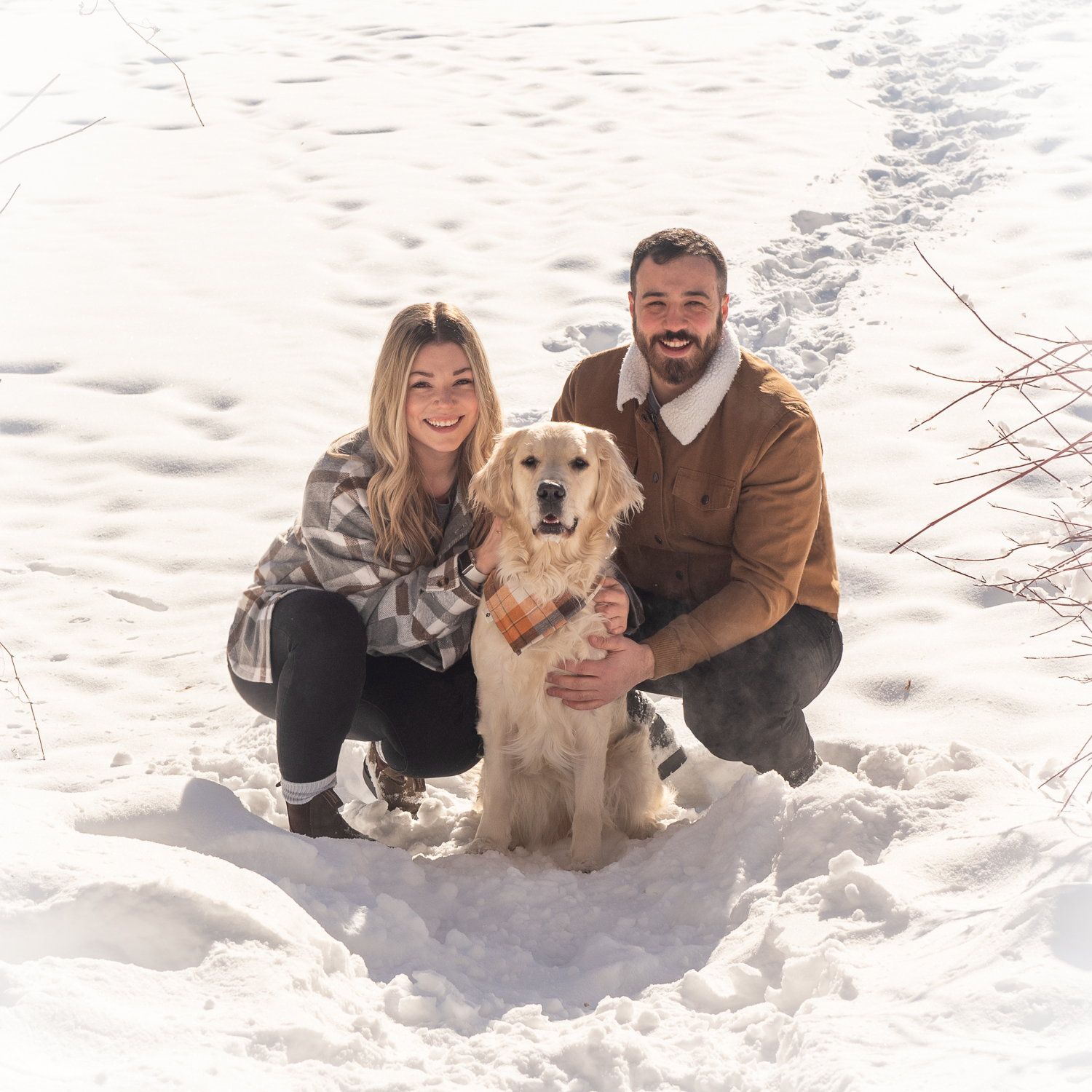 A couple crouching in deep snow with their golden retriever between them