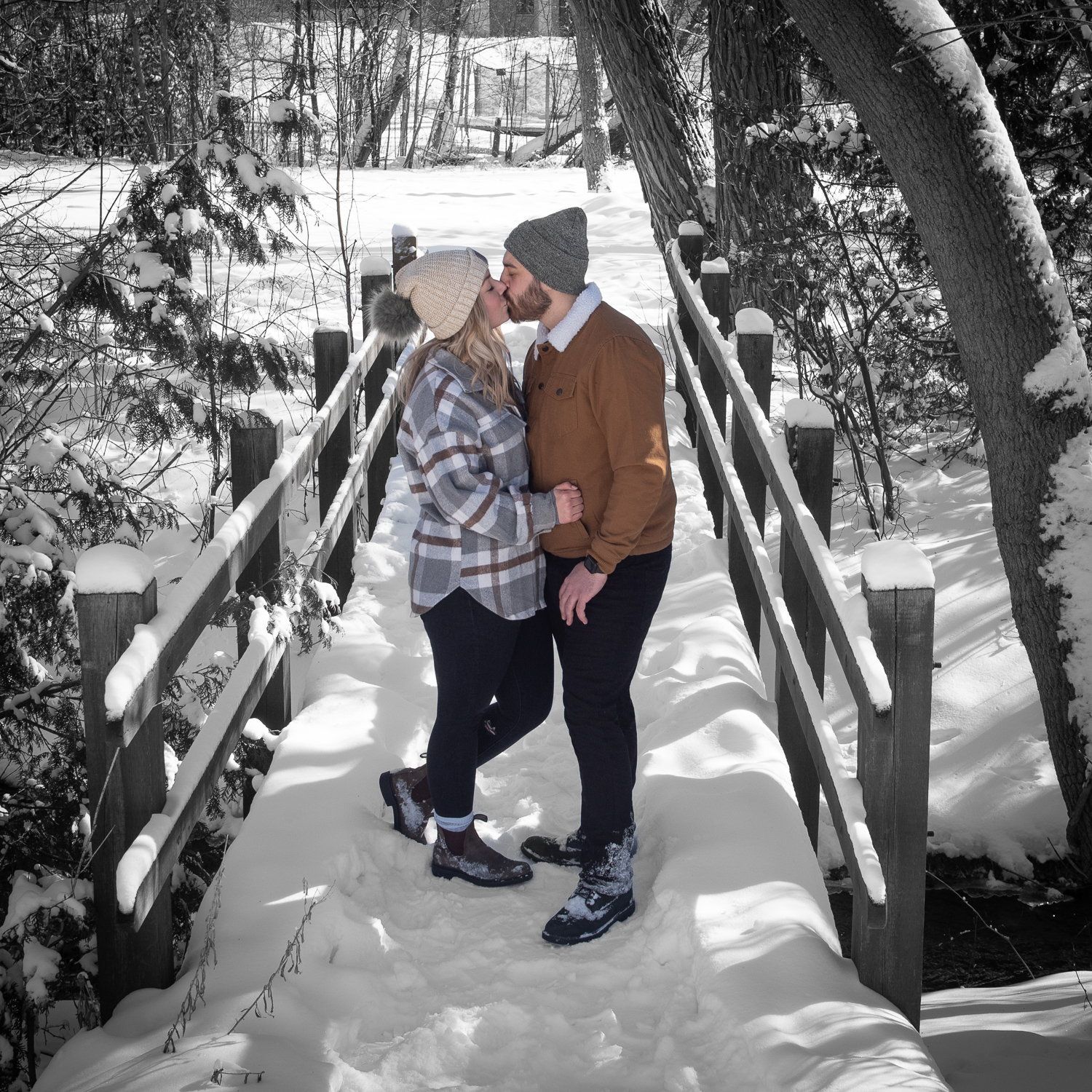 A couple kissing on a snow-covered wooden footbridge, their coats the only colour