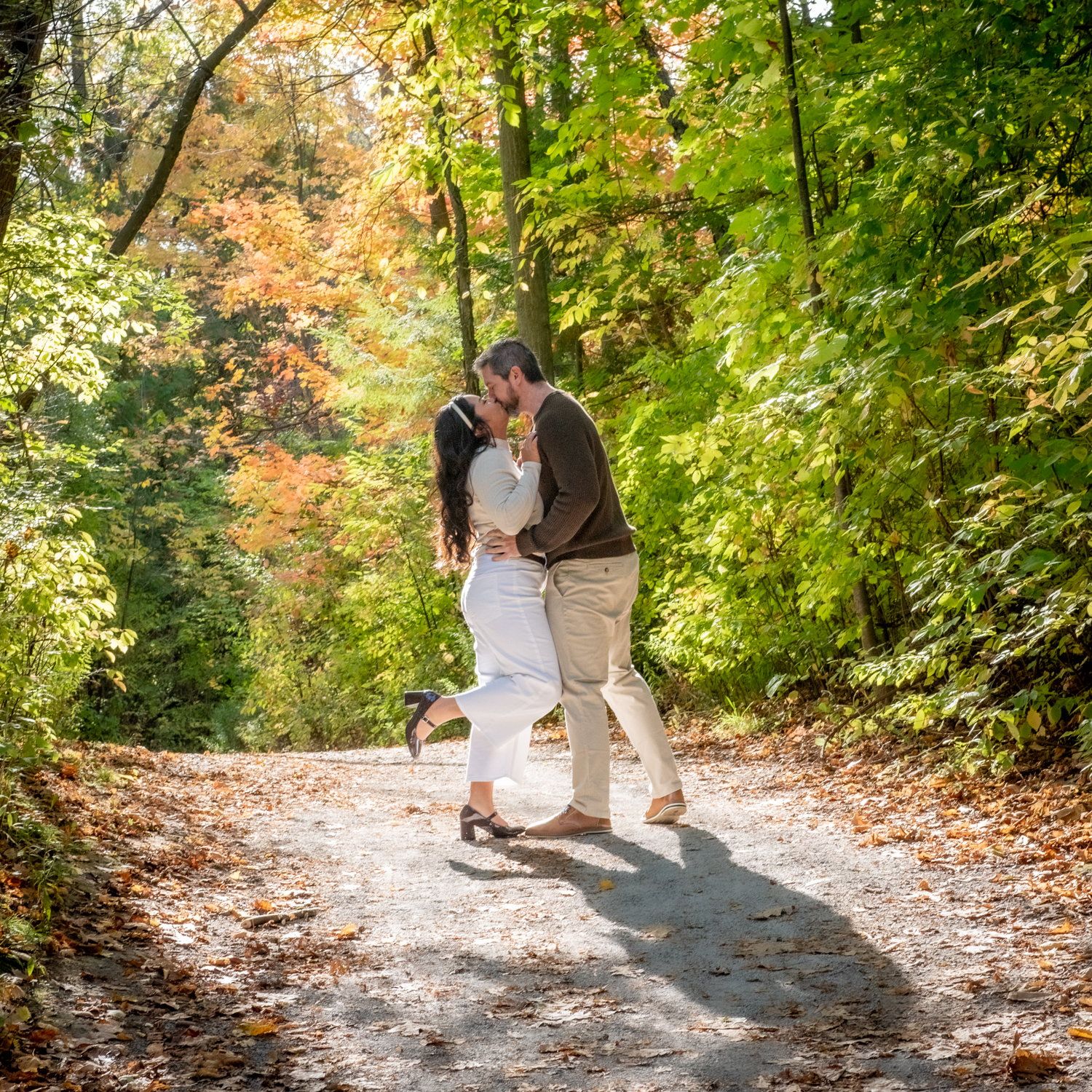 Justine & Josh kissing on a sunlit path in late-summer green