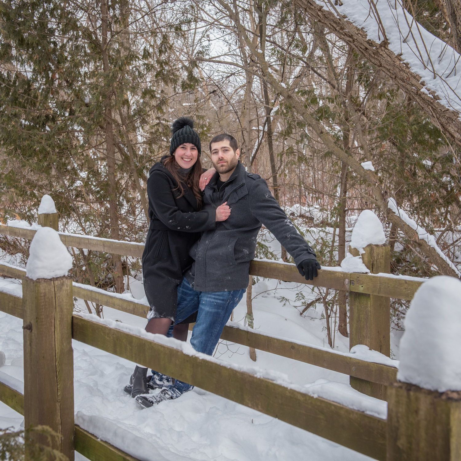 A couple leaning on a snow-covered split-rail fence