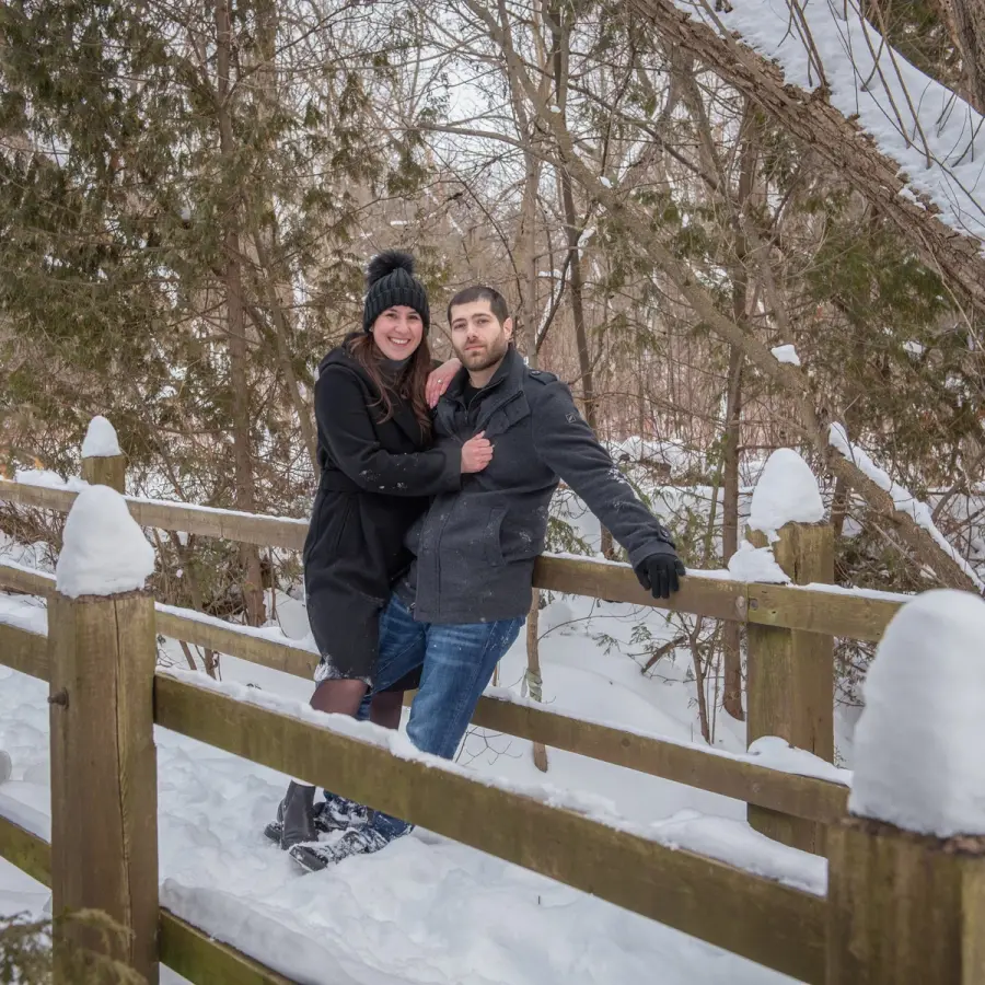 A couple leaning on a snow-covered split-rail fence