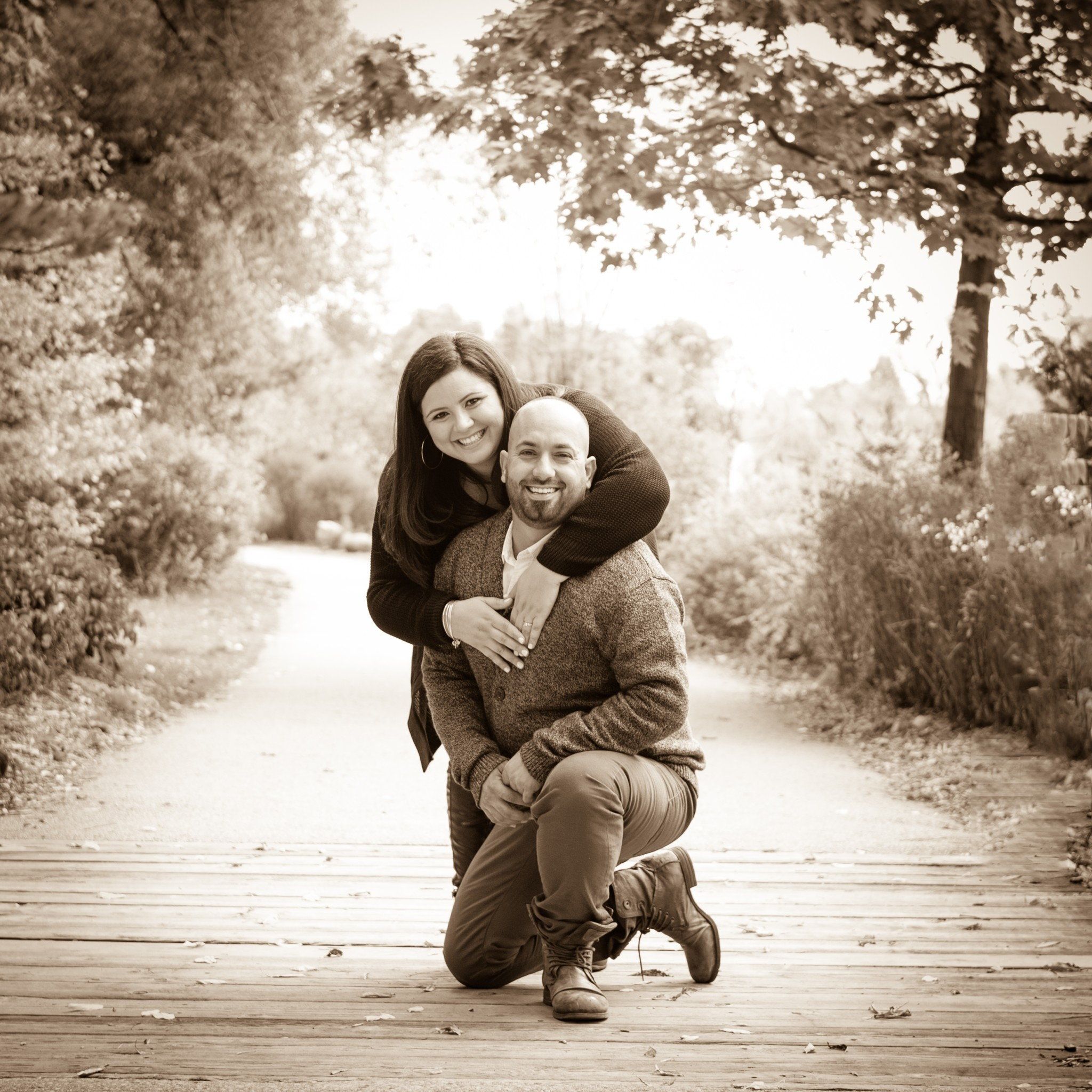 Sepia-toned photo of a man kneeling on a woodland path while his partner leans over him