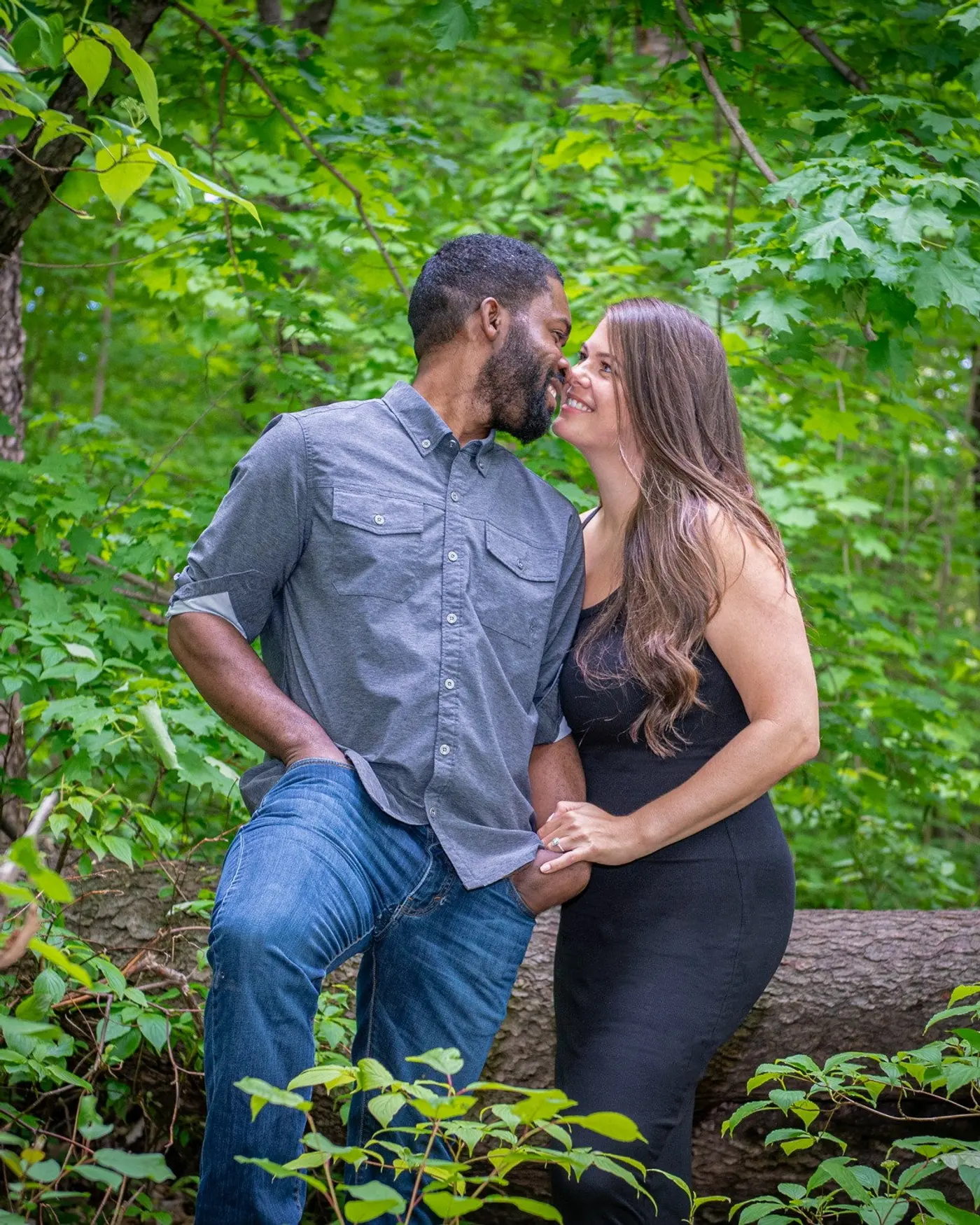 A couple leaning in close and laughing together in front of summer-green maples