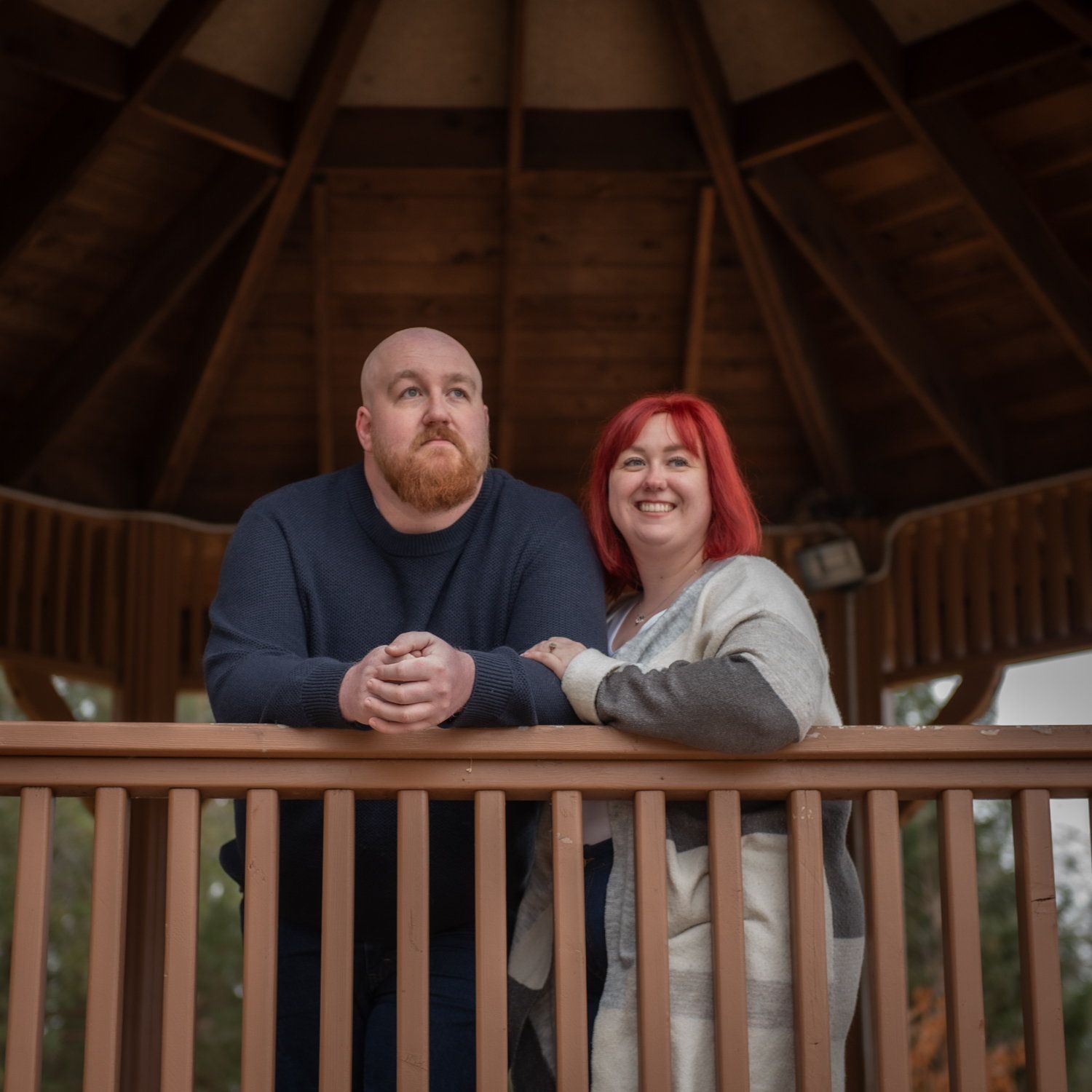 A couple leaning on the rail of a wooden gazebo, looking out