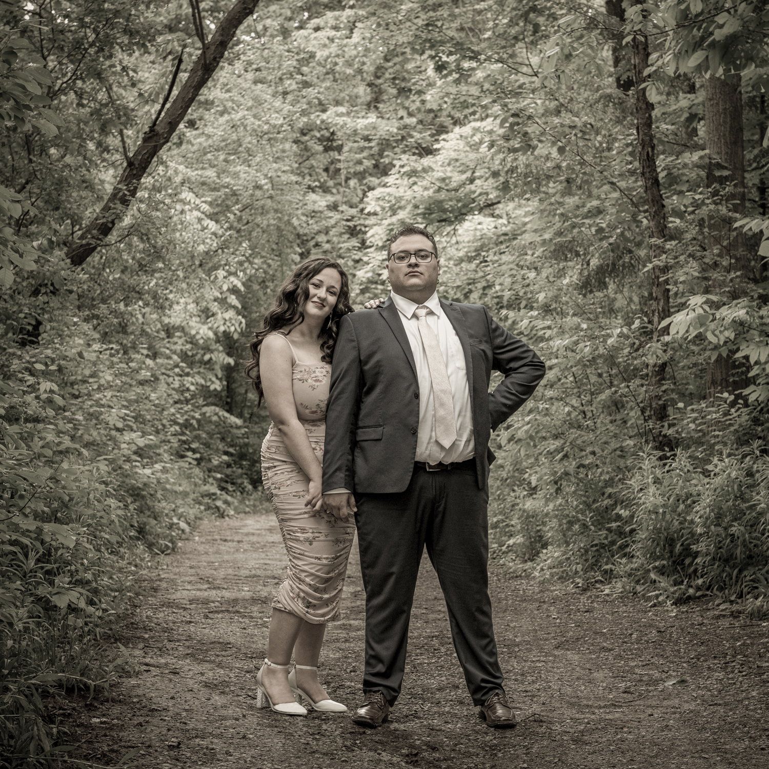 Black-and-white photo of a couple in formal dress standing on a wooded park path