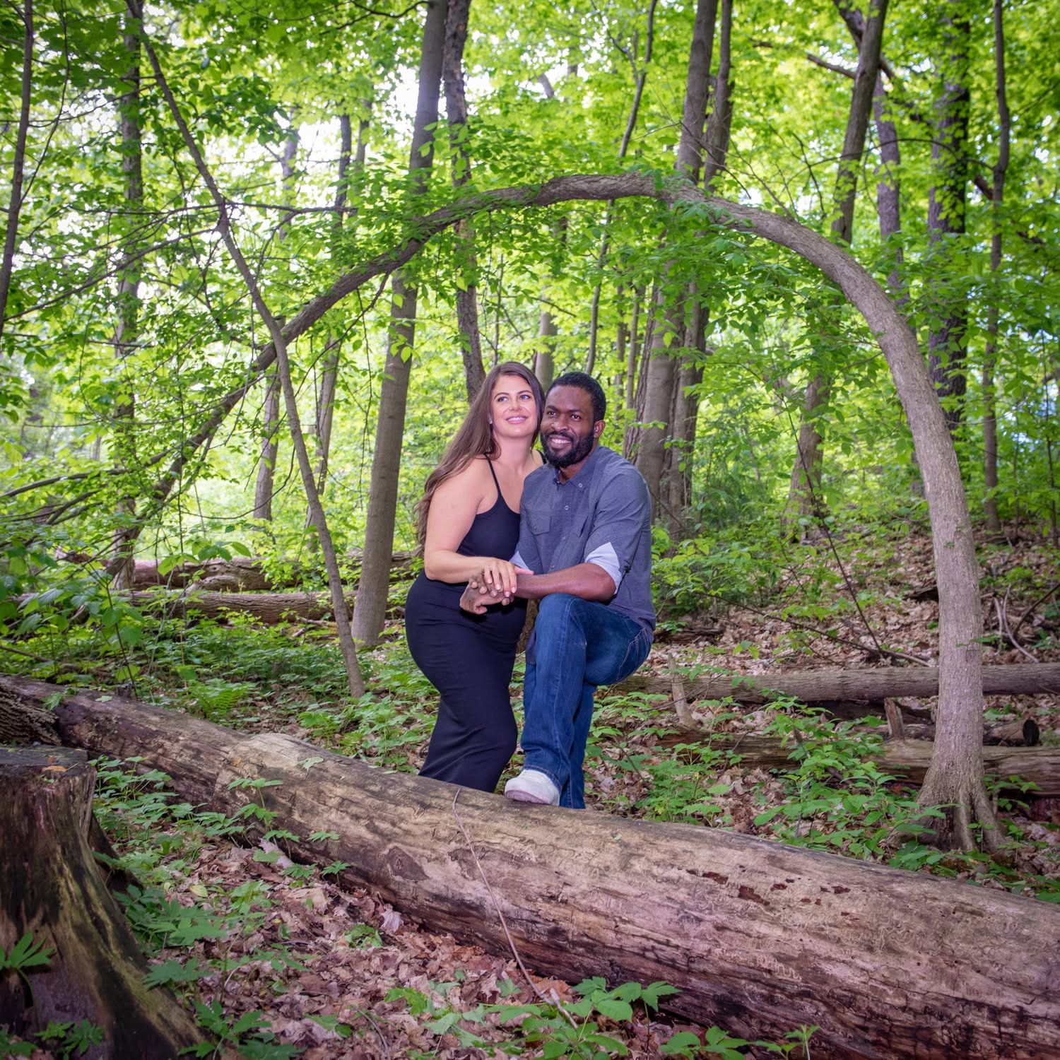 A couple seated on a fallen log under an arching branch in spring woodland
