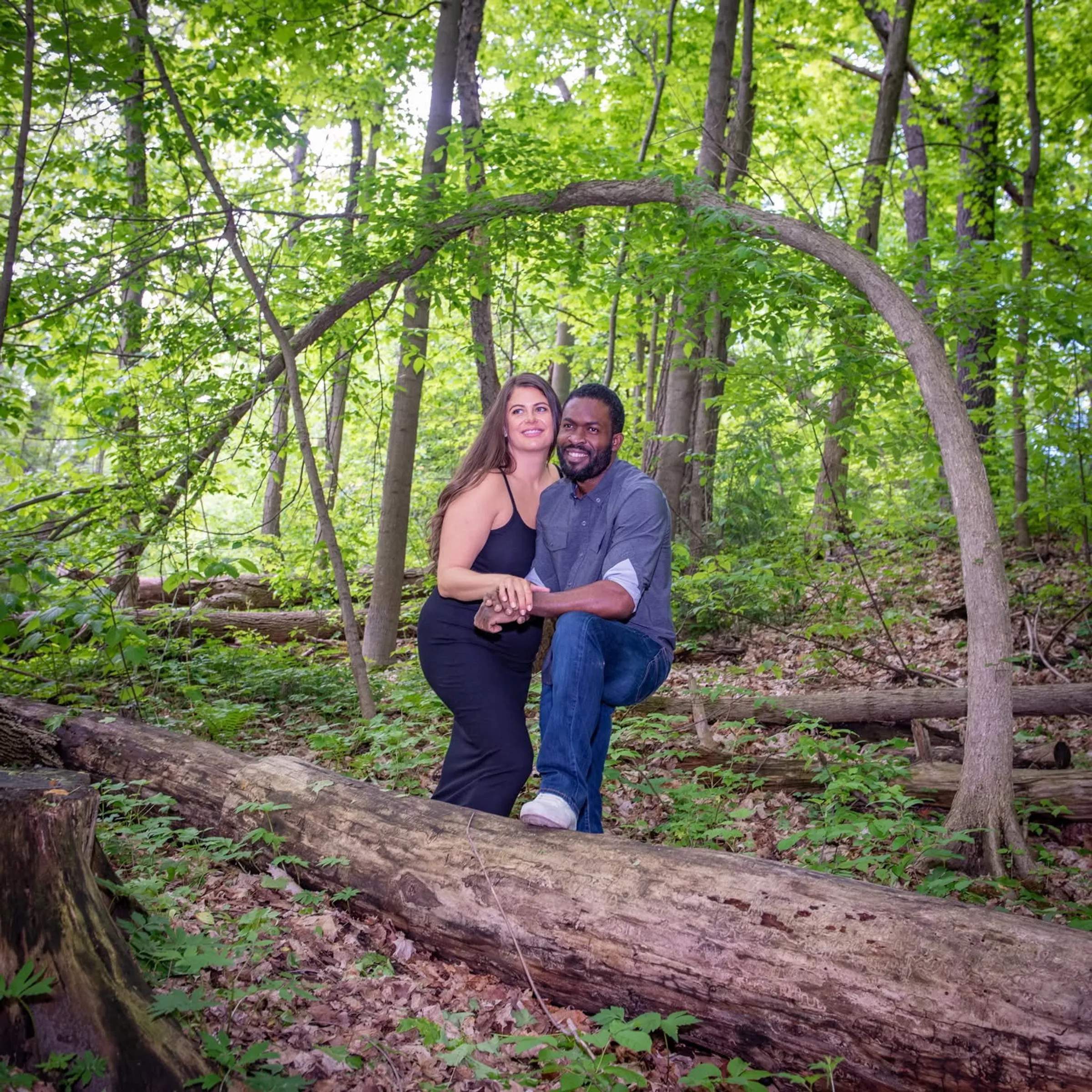 A couple seated on a fallen log under an arching branch in spring woodland